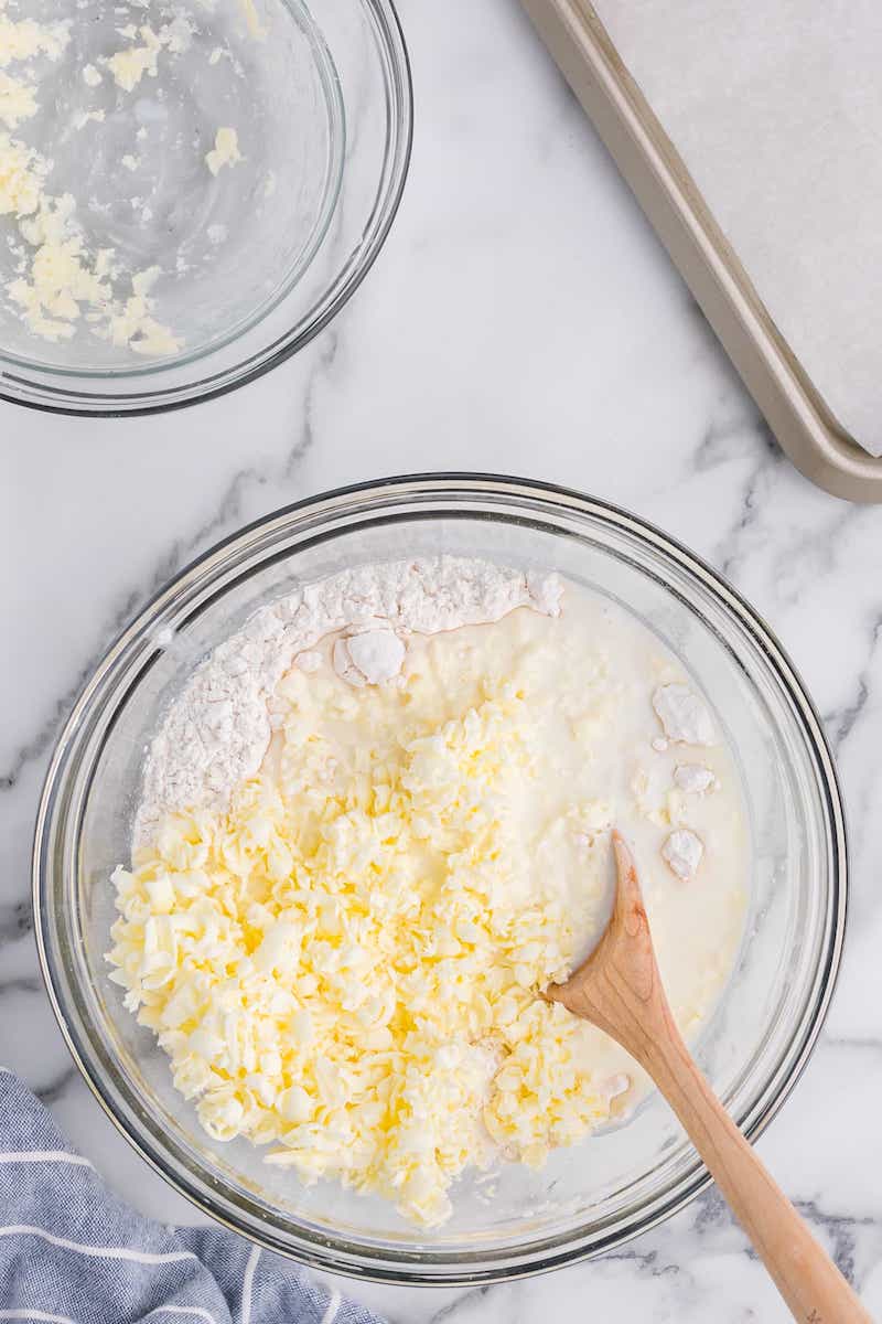 whisking grated butter, self rising flour, and buttermilk in a bowl for 3 ingredient buttermilk biscuits.