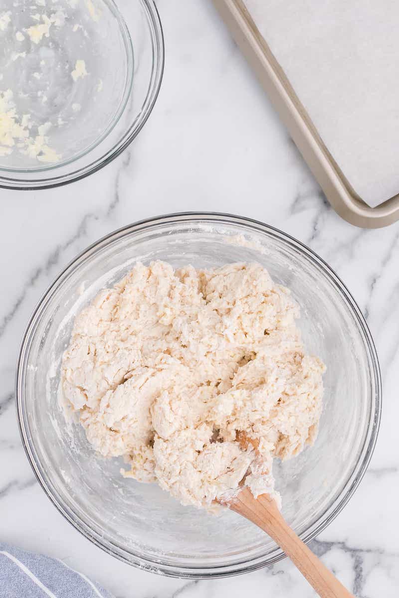 Using wooden spoon to mix sticky dough in a glass mixing bowl.