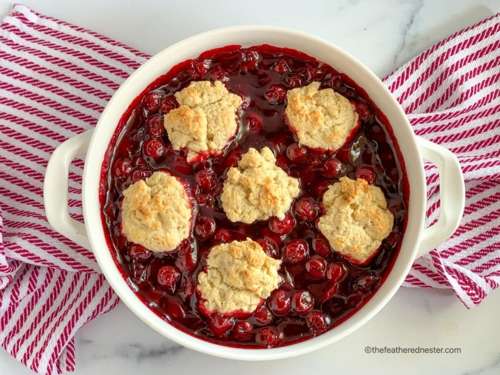 a casserole of easy cherry cobbler with cherry pie filling on top of a red and white napkin ready to serve