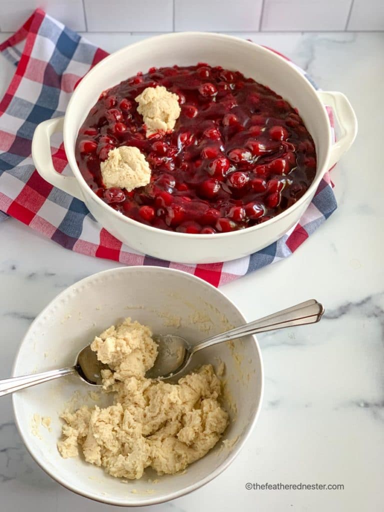 a bowl of biscuit topping and Bisquick cherry cobbler in a casserole dish being prepared in the background