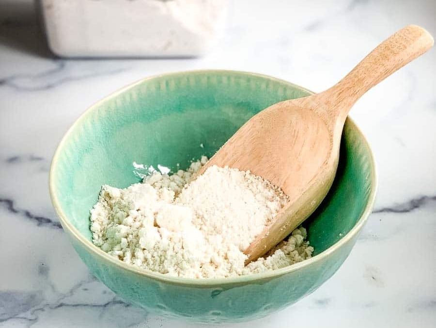 a bowl of DIY baking mix with a wooden scoop and a canister of homemade Bisquick mix in the background.