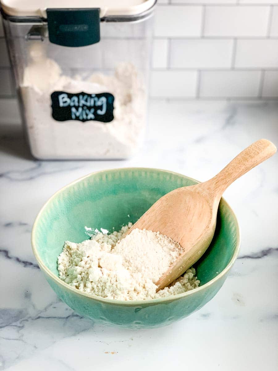 a bowl of DIY baking mix with a wooden scoop and a canister of homemade Bisquick mix in the background.