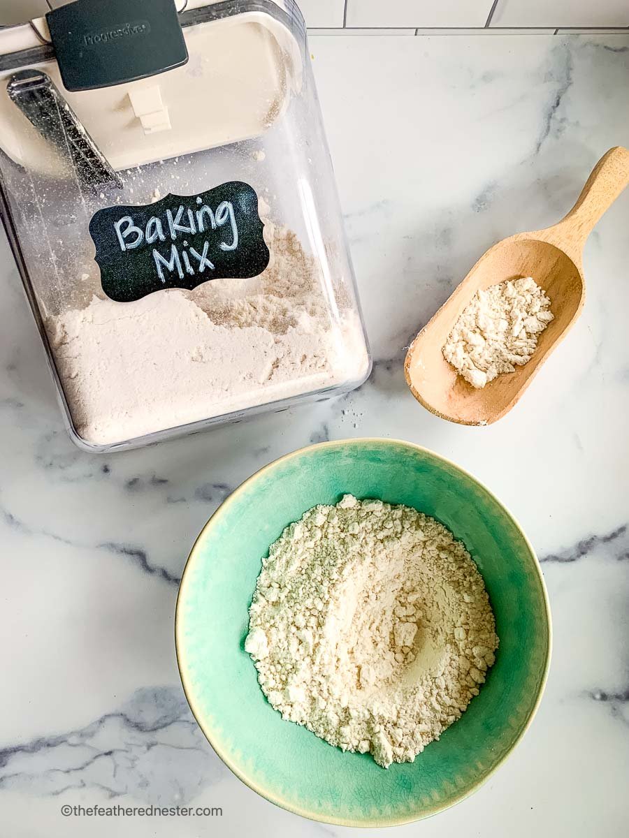 a green bowl of DIY baking mix with a Prepworks container of mixed homemade Bisquick baking mix and a wooden scoop of the scratch mix.