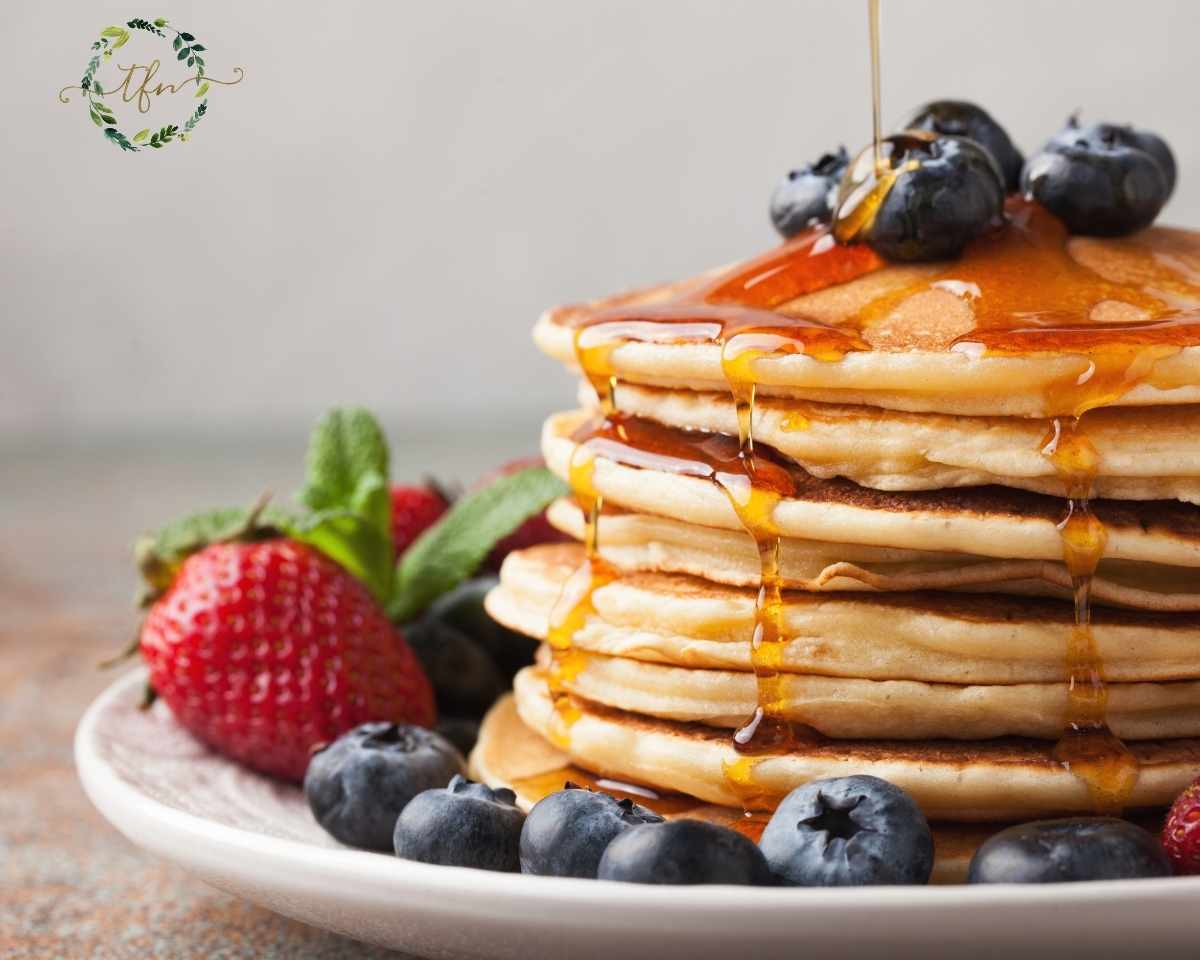 Strawberries and blueberries with a stack of ultimate pancakes with syrup being drizzled over.