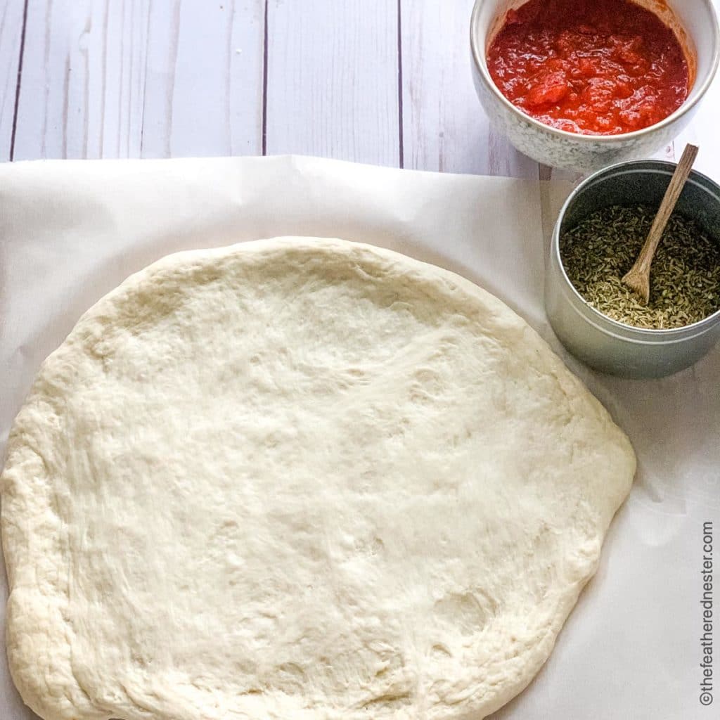 A rolled out circle of pizza dough laid on parchment paper.