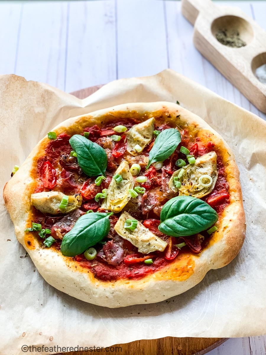 baked vegan pizza with marinara sauce, artichokes, bell pepper, and cherry tomatoes and fresh basil on top.