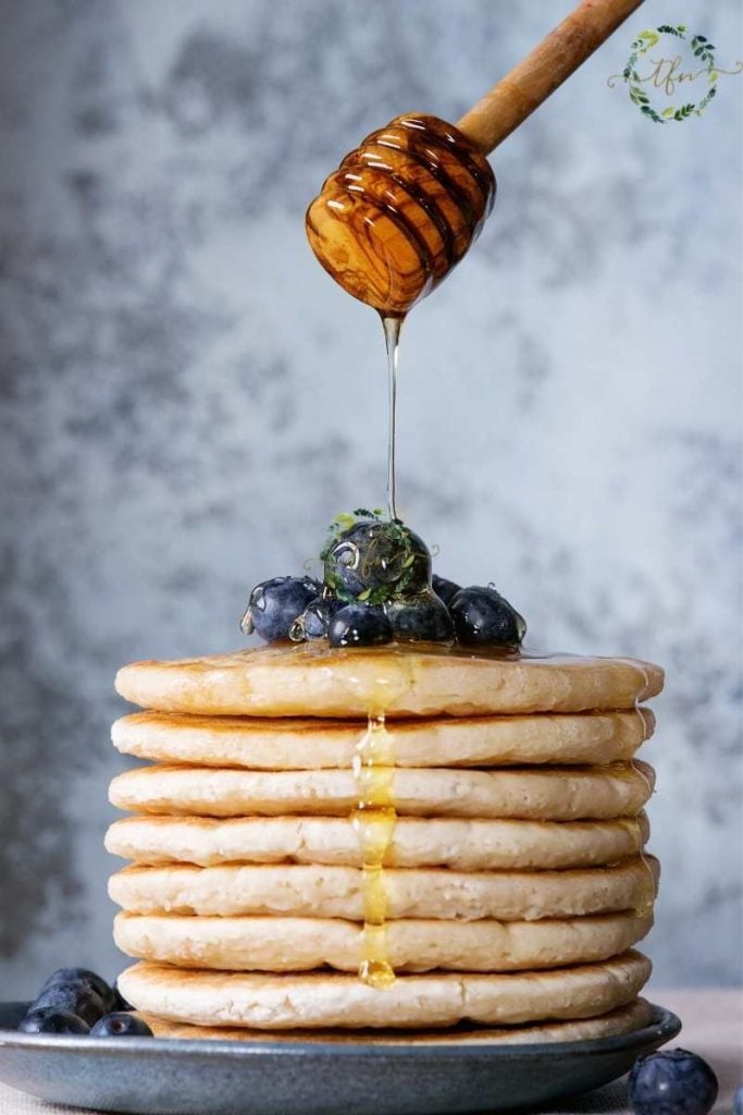 Honig über einen Stapel Bisquick-Hotcakes (Pfannkuchen) und Blaubeeren träufeln