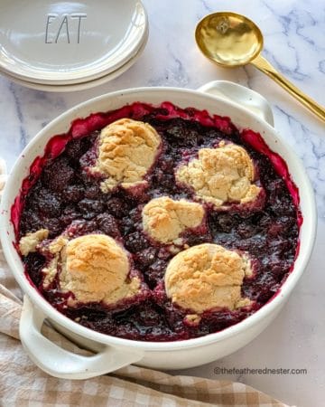 a white casserole dish of blackberry cobbler ready to serve