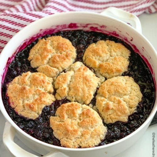 a round casserole dish of blueberry cobbler with a red and white napkin