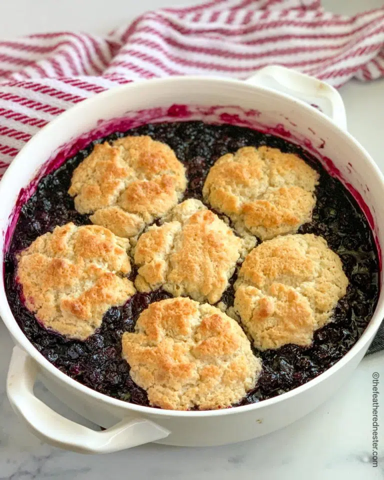 a round casserole dish of blueberry cobbler with a red and white napkin