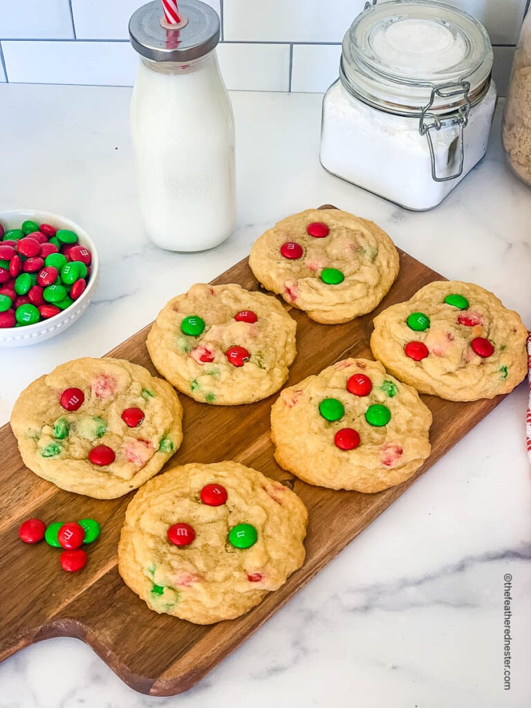 mm cookies on a wooden board with a jar of milk and a bowl of m and ms in the background
