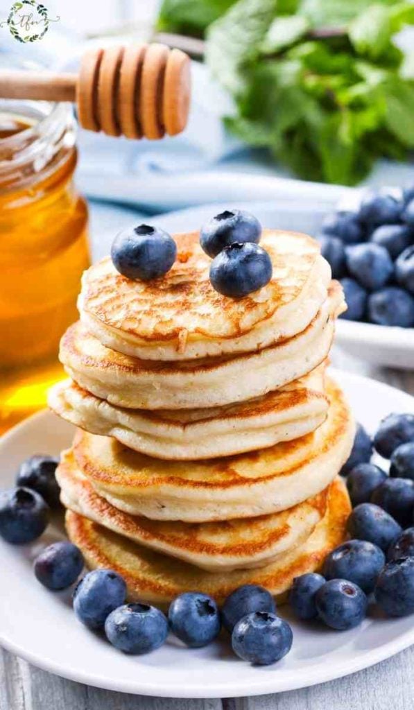 Dripping honey onto plate of fluffy hotcakes topped with fresh blueberries