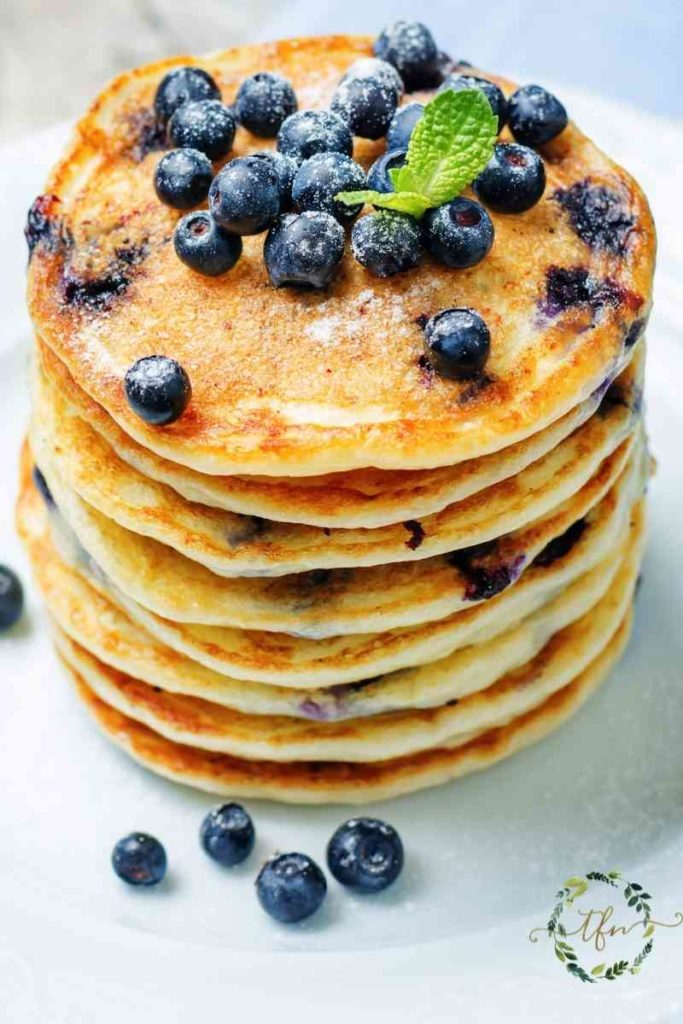 Stack of 8 blueberry sourdough starter pancakes topped with more blueberries and fresh mint.
