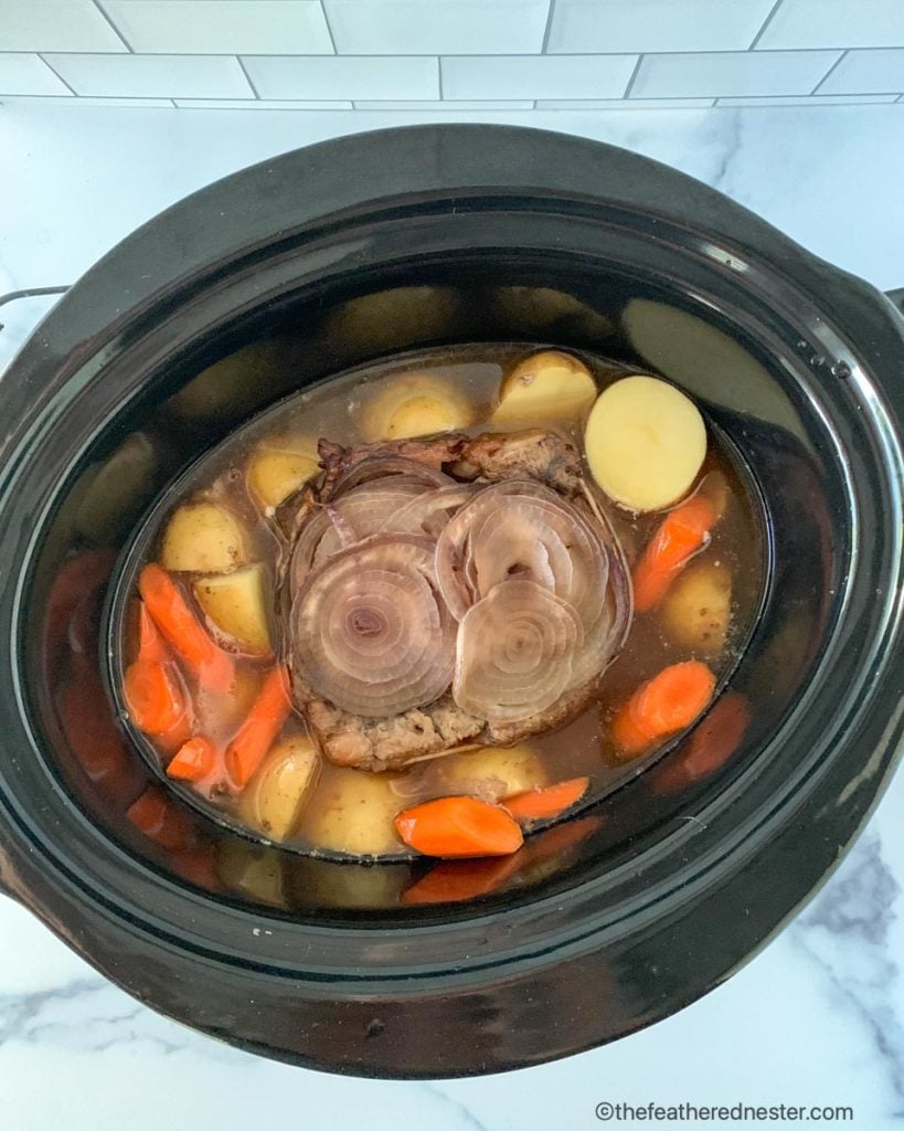 Adding the potatoes and carrots to the slow cooker pot during the last two hours of cooking