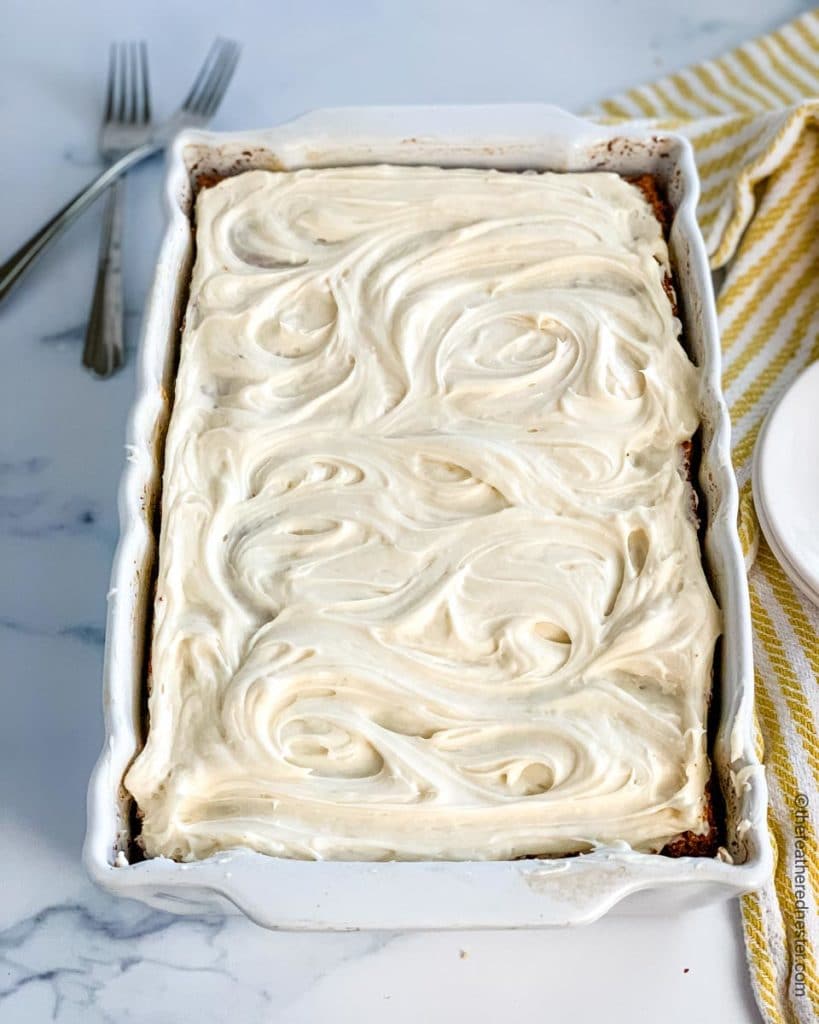 A pan of old fashioned apple cake topped with frosting sitting next to serving plates and forks.