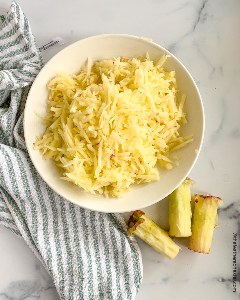 A bowl full of grated apples sitting on a gray and white striped kitchen towel.