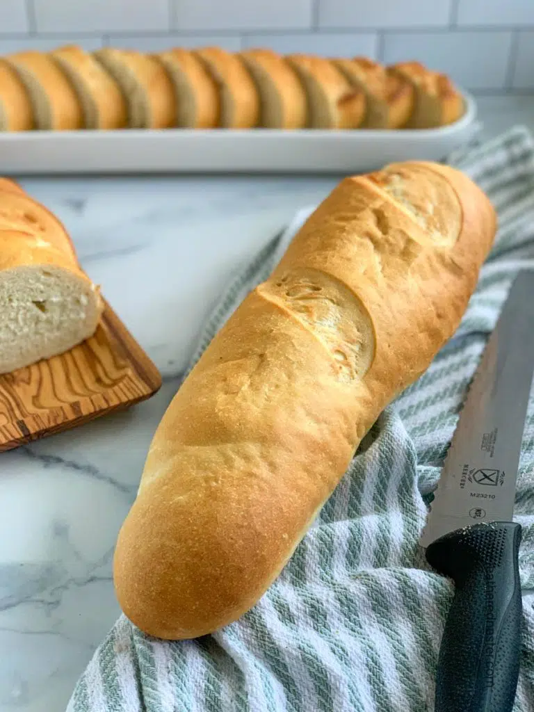 a loaf of sourdough French bread on a green and white napkin with sliced bread in the background