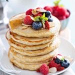 Tall stack of sourdough discard pancakes with syrup and fresh berries on top.