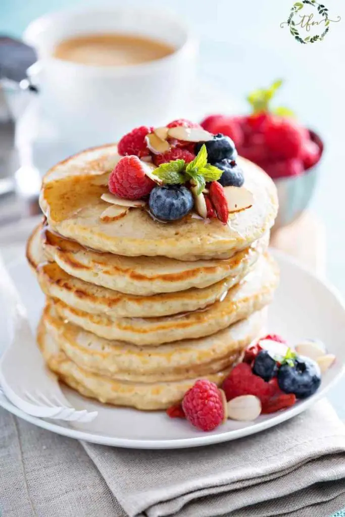 Tall stack of sourdough discard pancakes with syrup and fresh berries on top.