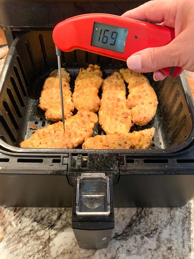 chicken strips in an air fryer with an instant read thermometer showing 169 degrees Fahrehheit