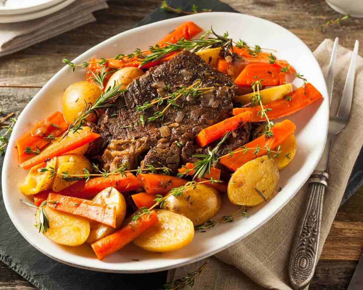 a plate with pot roast and vegetables with a serving platter in the background
