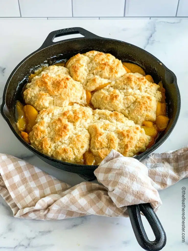 peach cobbler in a cast iron skillet with a tan and white napkin over the handle