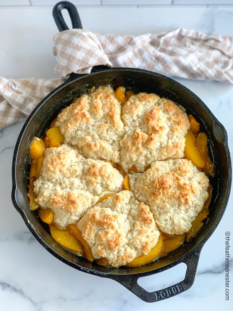 Baked Peach Cobbler in a Cast Iron Skillet with a tan and white checked napkin.