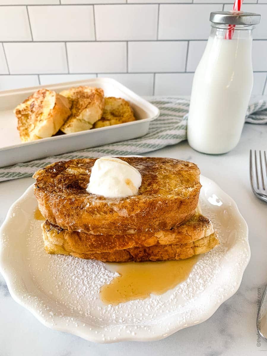 A white plate of French toast with butter and syrup over the top. A bottle of milk in the background.