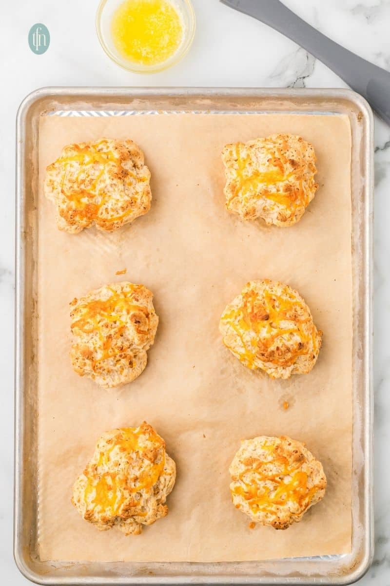 Cheddar biscuits on a baking sheet with parchment paper.