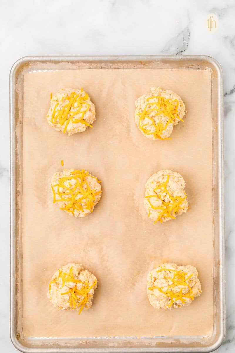 Cheddar biscuit batter ball on a baking sheet with parchment paper.