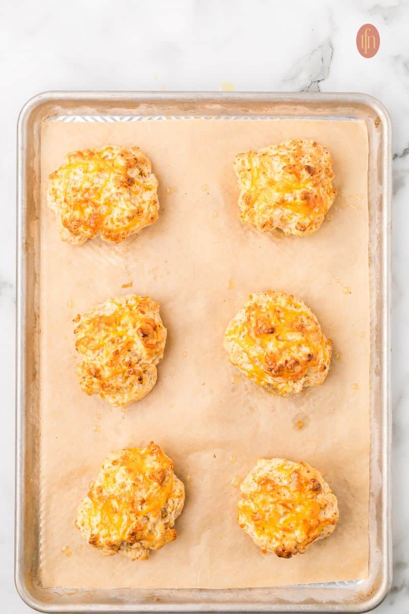Cheddar biscuits on a baking sheet with parchment paper.