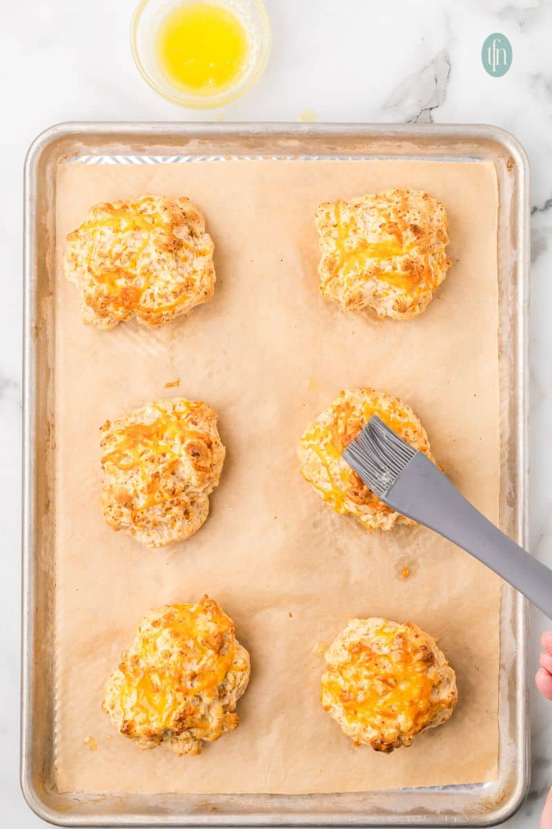 Cheddar biscuits brushed with butter on a baking sheet with parchment paper.