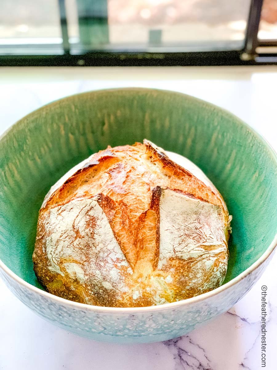 A loaf of overnight sourdough bread in a green bowl.