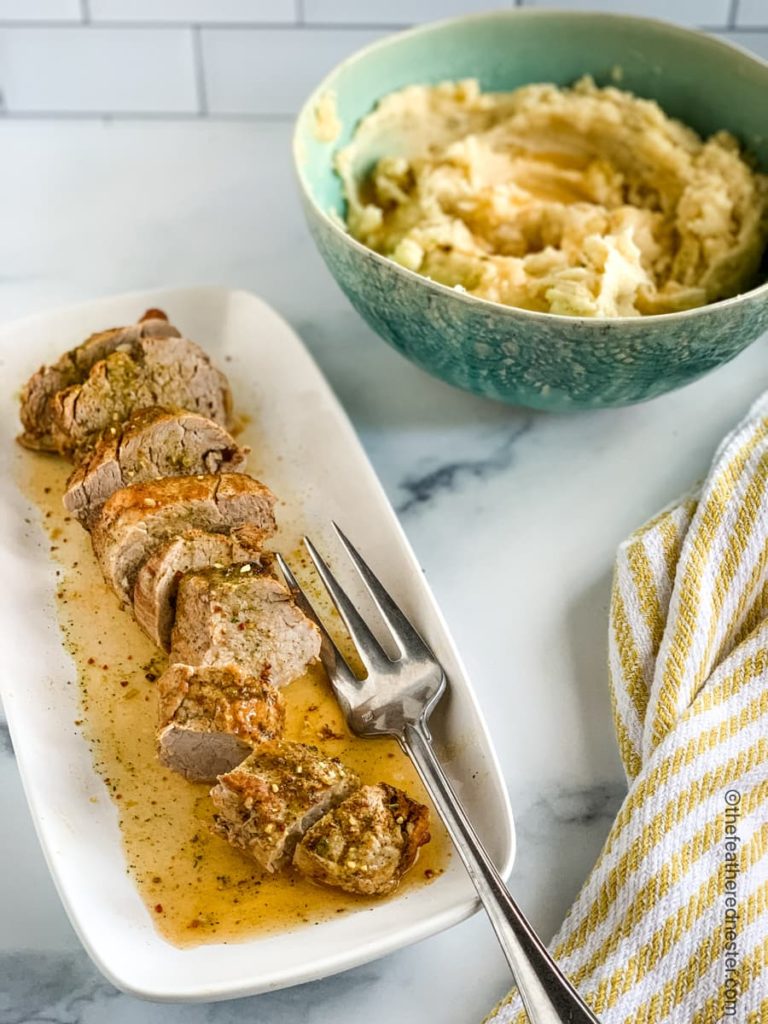 a white platter of sliced pork tenderloin and a green bowl of mashed potatoes with a yellow and white napkin