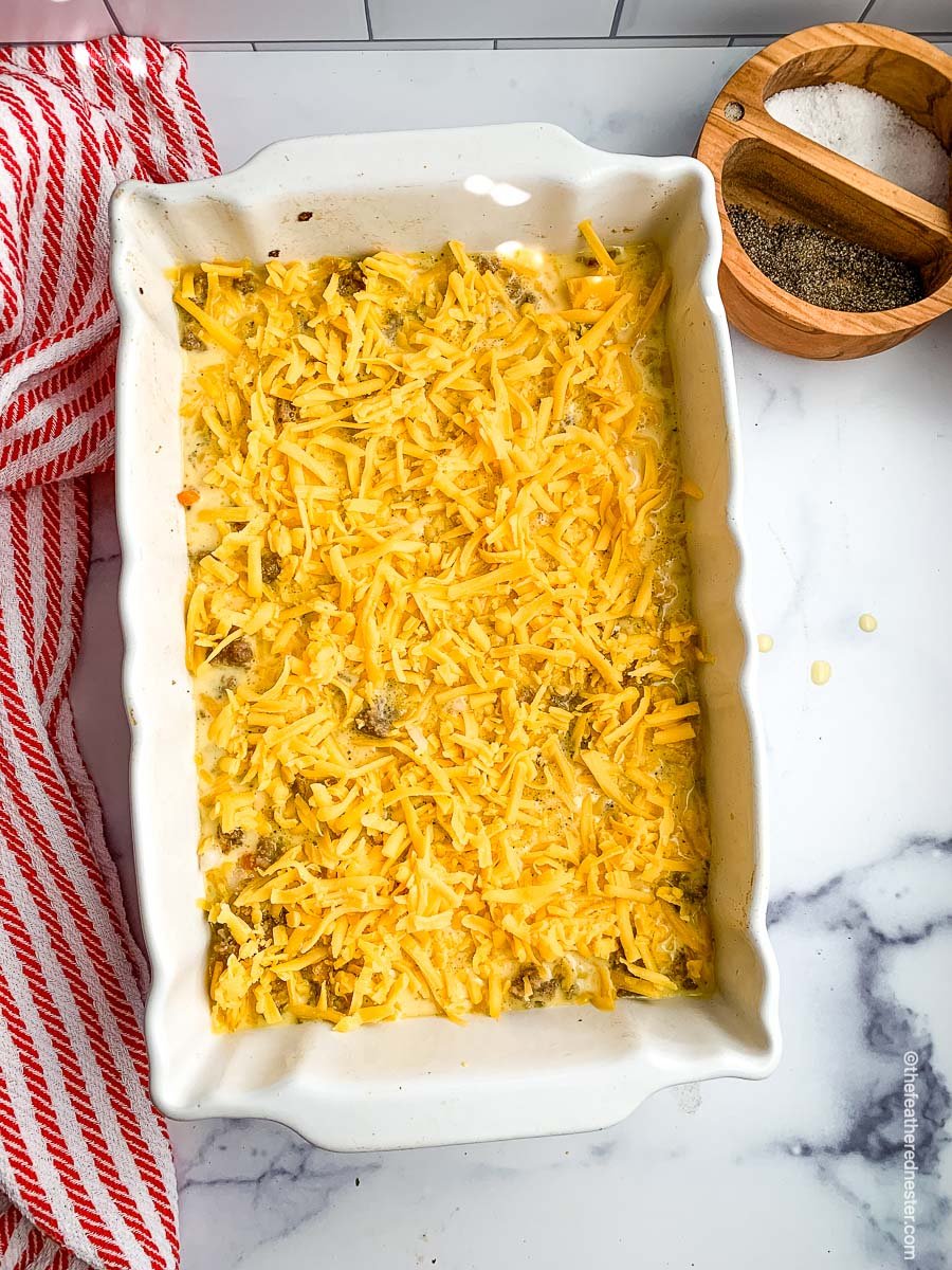 a casserole dish of potatoes and shredded cheese ready to bake.