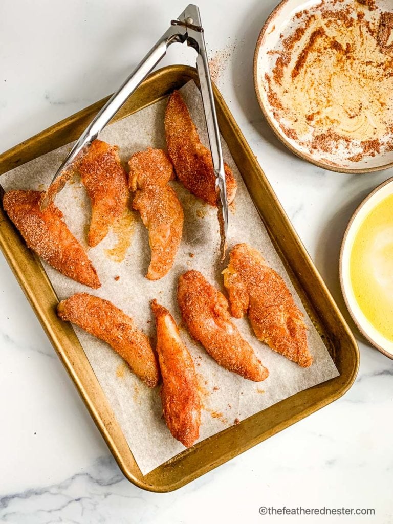  une plaque à pâtisserie de tenders de poulet trempés (sans panure) et des assiettes de beurre et d'assaisonnements 