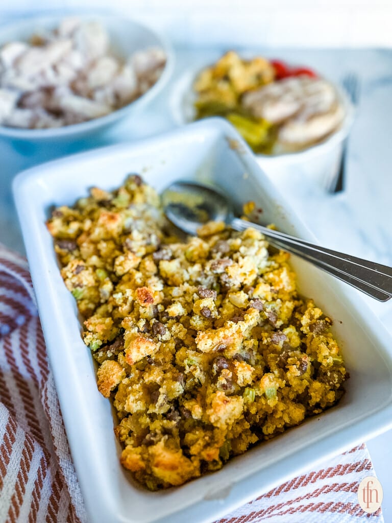 Cornbread dressing in a white dish with a silver spoon on the side.