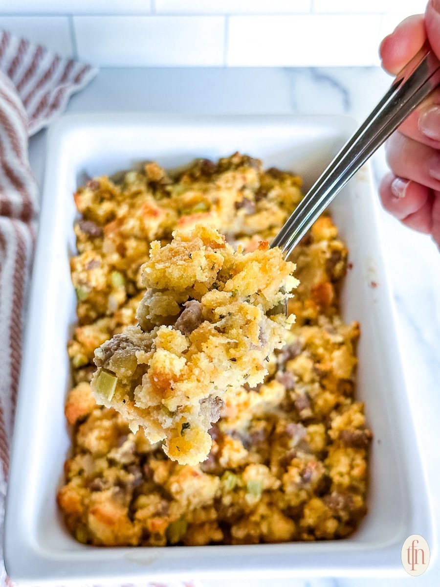 Lifting a scoop of casserole up with a spoon over a white dish.