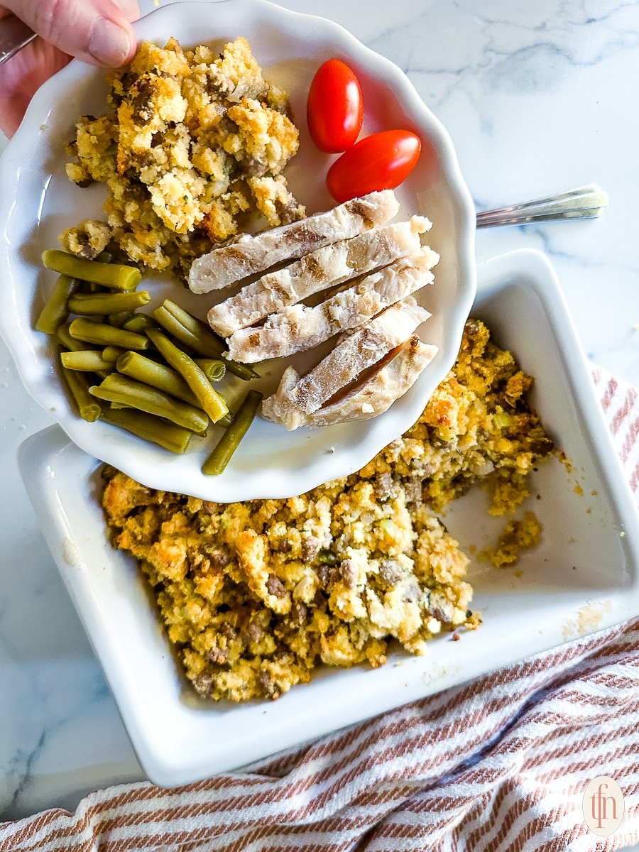 Plate of sliced meat, green beans, dressing, and tomatoes over a dish of cornbread.