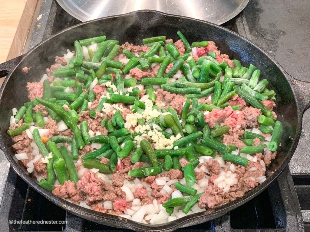 a skillet of ground beef, green beans, and onions sautéing