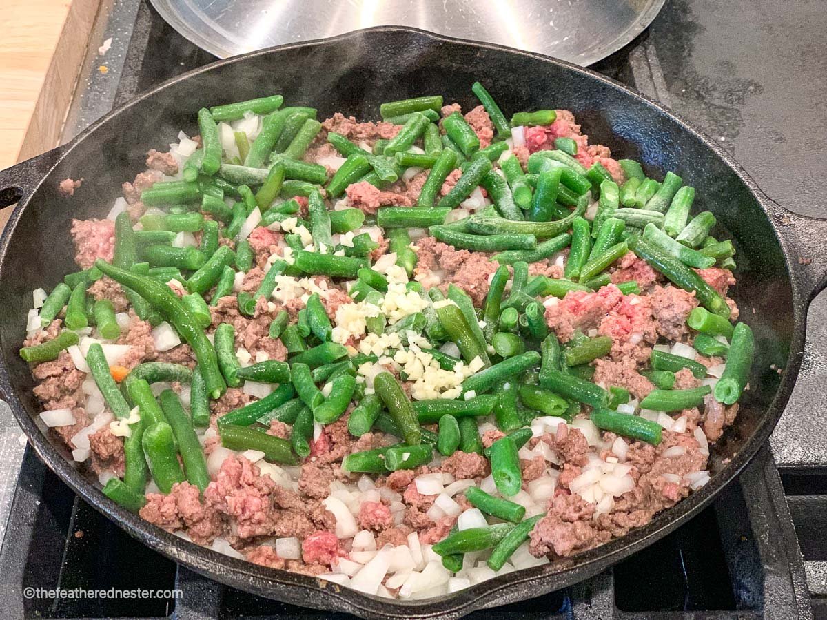 a skillet of ground beef, green beans and onions sautéing.