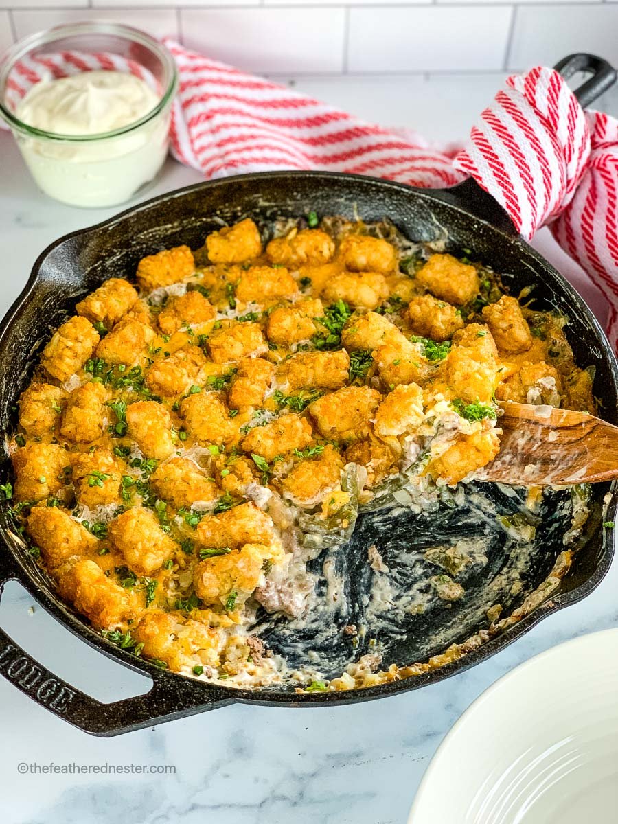 a cast iron skillet with green bean casserole with tater tots.