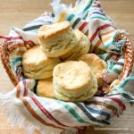 a basket full of buttermilk biscuits with a striped napkin