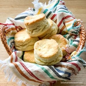 Flaky buttermilk biscuits in a basket lined with a striped napkin.