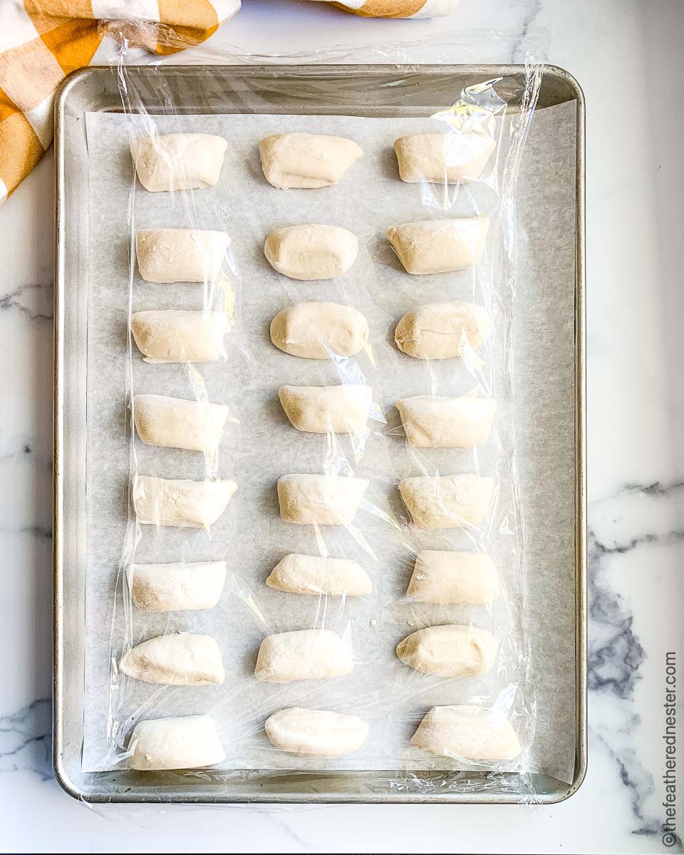 a cookie sheet of parker house rolls frozen, covered with plastic wrap for defrosting and rising.