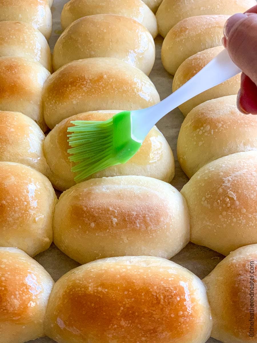 Brushing melted butter over homemade bread rolls.