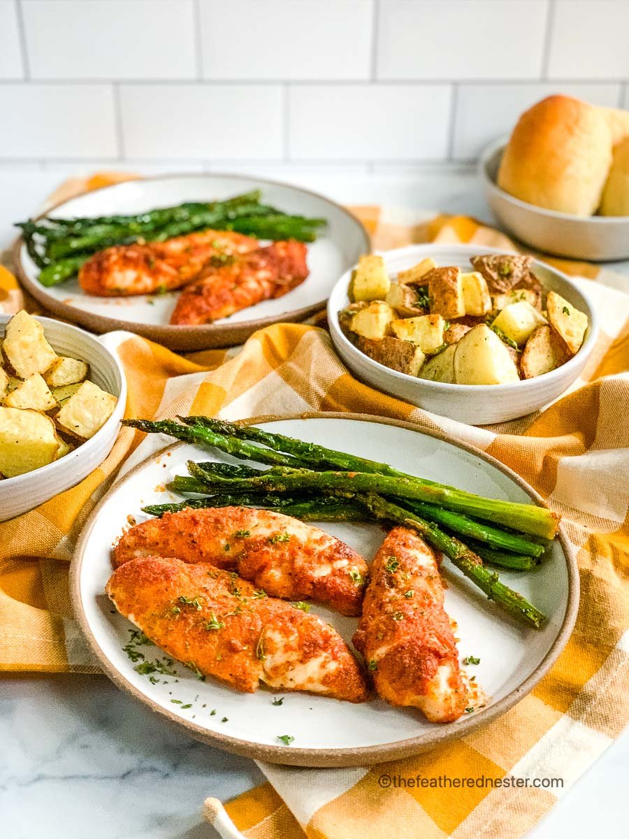 plates of baked chicken tenderloins with asparagus and potatoes ready to serve.