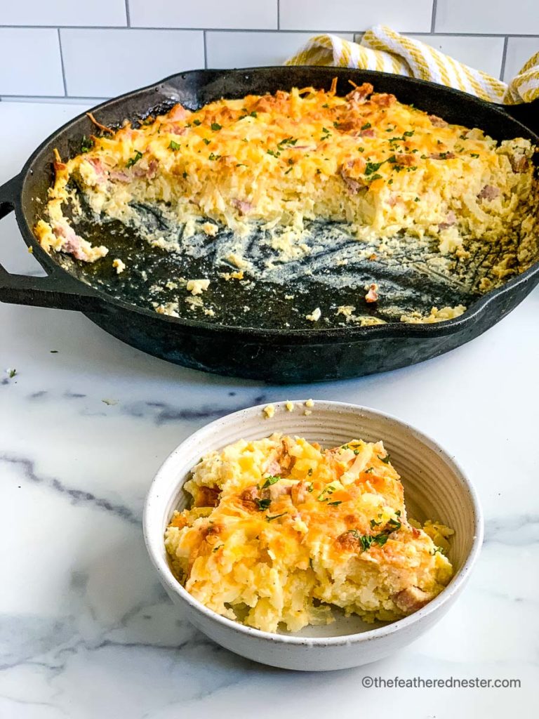 a bowl of breakfast casserole with the skillet of the casserole in the background