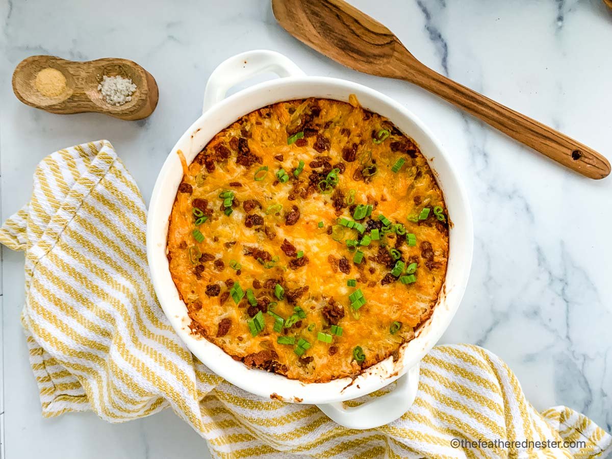 bacon hash brown casserole in a white serving dish with a spoon and spices.