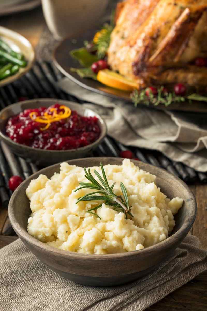 A bowl of mashed potatoes with a turkey in the background.